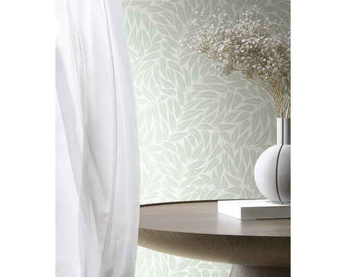 Vliesbehang met bladpatroon in een lichte kamer met houten tafel, bloemenvaas en gordijn.