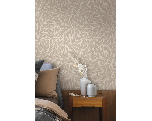 Behang met bladmotief in een slaapkamer boven een nachtkastje met vazen en droogbloemen naast een bed.
