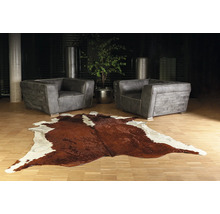 Moderne woonkamer met twee grijze leren fauteuils en een bruin-wit koeienhuid vloerkleed op een lichte houten vloer.