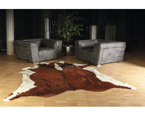 Moderne woonkamer met twee grijze leren fauteuils en een bruin-wit koeienhuid vloerkleed op een lichte houten vloer.