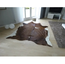 Natuurlijk gevormd koeienhuid vloerkleed in een lichte, modern ingerichte woonkamer met een lichte parketvloer.