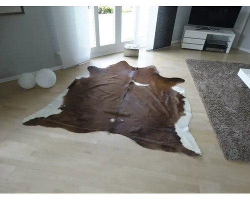 Natuurlijk gevormd koeienhuid vloerkleed in een lichte, modern ingerichte woonkamer met een lichte parketvloer.