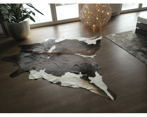 Koeienhuid vloerkleed van echt leer in een modern ingerichte woonkamer met houten vloer.