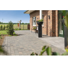 Ruim terras met betonnen klinkers voor een bakstenen huis, inclusief tuinbank en decoratieve plantenbak.