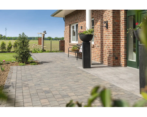 Ruim terras met betonnen klinkers voor een bakstenen huis, inclusief tuinbank en decoratieve plantenbak.