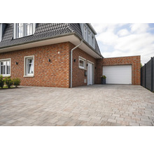 Exterieur van een bakstenen huis met een witte garagedeur en een grote oprit bestraat met rechthoekige stenen.