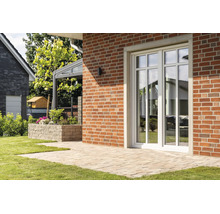 Witte terrasdeur met roedes in een rode bakstenen muur voor een betegeld terras in de tuin.