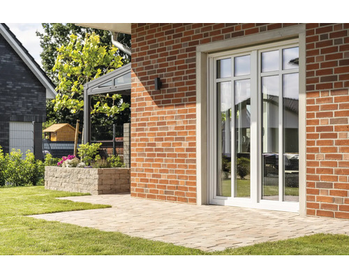 Witte terrasdeur met roedes in een rode bakstenen muur voor een betegeld terras in de tuin.