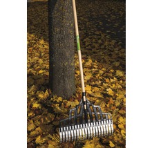 Kunststof bladhark met houten steel staat tegen een boom te midden van herfstbladeren.