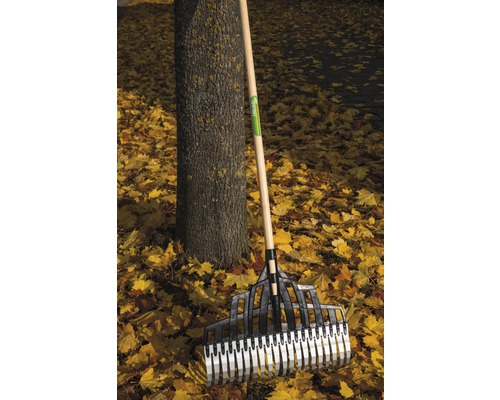 Kunststof bladhark met houten steel staat tegen een boom te midden van herfstbladeren.