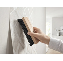 Hand strijkt behang met patroon glad met een houten behangborstel.