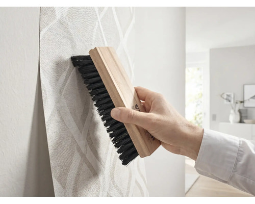 Hand strijkt behang met patroon glad met een houten behangborstel.