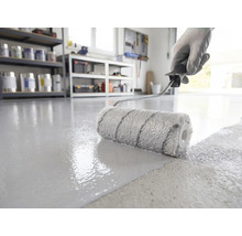 Vloercoating wordt met een verfroller aangebracht op een betonnen vloer in een lichte, georganiseerde werkplaats.