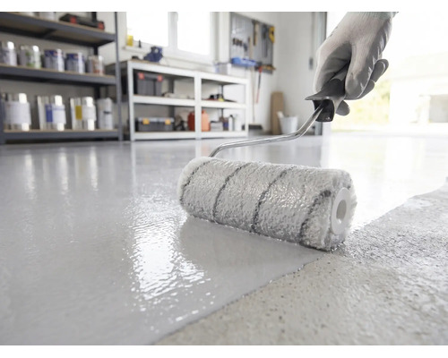 Vloercoating wordt met een verfroller aangebracht op een betonnen vloer in een lichte, georganiseerde werkplaats.