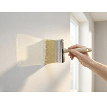 Een hand brengt witte muurverf aan op een muur met een brede blokkwast.