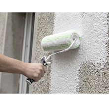 Een hand schildert een gevel met grove structuur met een gevelroller.