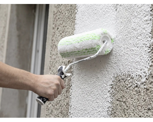 Een hand schildert een gevel met grove structuur met een gevelroller.