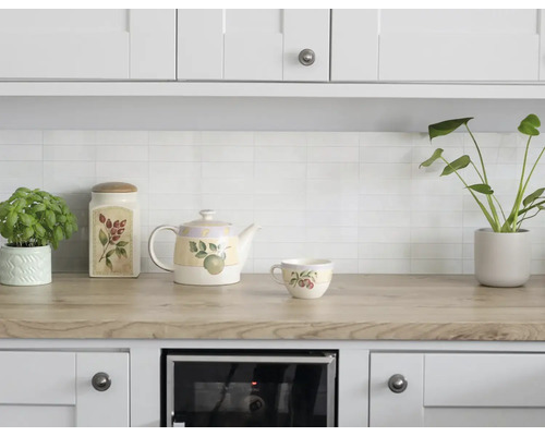 Lichte keuken met houten aanrechtblad, witte wandtegels, keramische theepot, kopje en voorraadpot met botanische prints en planten.