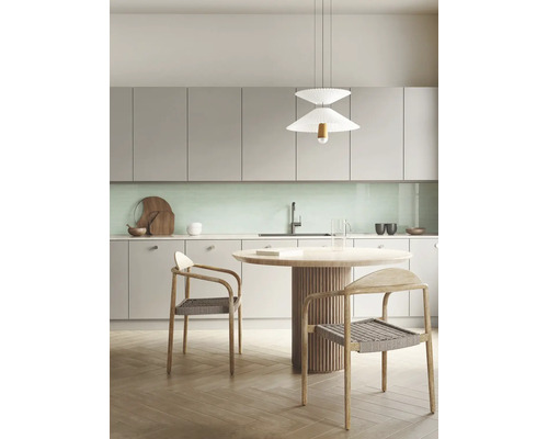 Moderne keuken met lichtgrijze kasten, mintgroene achterwand, ronde houten tafel en gevlochten stoelen onder een witte hanglamp.