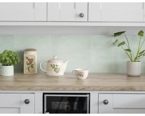 Licht ingerichte keuken met lichtgroene mozaïek tegels als achterwand, werkblad in houtlook en witte kasten.