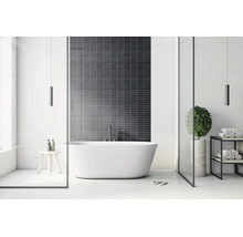 Moderne, lichte badkamer met een vrijstaand bad voor een wand met donkere tegels, een minimalistisch rek en een houten krukje.