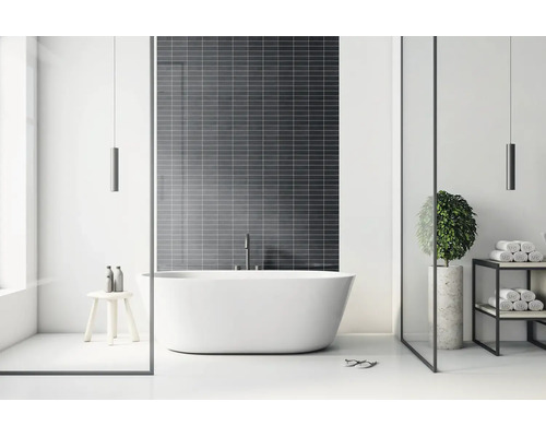 Moderne, lichte badkamer met een vrijstaand bad voor een wand met donkere tegels, een minimalistisch rek en een houten krukje.