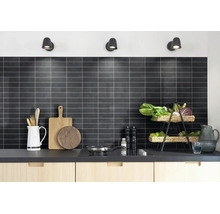 Moderne keuken met een achterwand van donkere rechthoekige tegels en lichte voegen. Op het aanrecht staan keukengerei en een fruitmand.