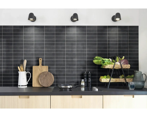 Moderne keuken met een achterwand van donkere rechthoekige tegels en lichte voegen. Op het aanrecht staan keukengerei en een fruitmand.