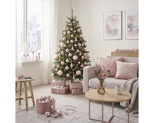 Lichte woonkamer met versierde kerstboom, roze kerstballen, cadeaus, grijze bank met kussens en een salontafel.