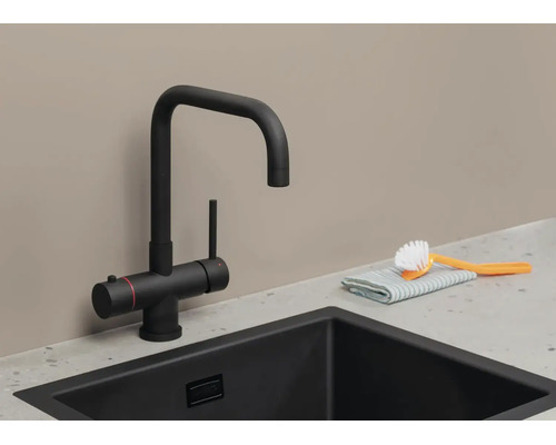 Zwarte mat keukenmengkraan met U-uitloop en kokendwaterfunctie bij een zwarte spoelbak met schoonmaakaccessoires.