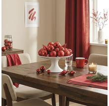 Feestelijk gedekte houten tafel met een witte etagère vol rode kerstballen, een kaars en adventsdecoratie.