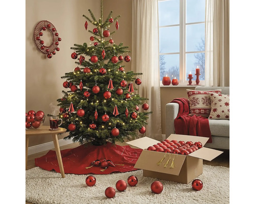Feestelijk versierde kerstboom met rode ballen en LED-verlichting in een sfeervolle woonkamer met bank en kerstdecoratie.