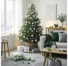 Licht ingerichte woonkamer met versierde kerstboom in rieten mand, bank en houten salontafel met kerstballen en cadeaus.
