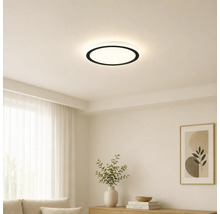 Moderne ronde LED-plafondlamp met zwarte rand in een lichte, minimalistische woonkamer met witte muren en lichte meubels.