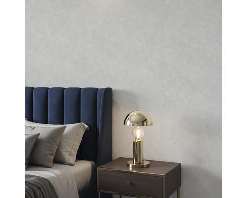 Goudkleurige tafellamp op een nachtkastje in een slaapkamer met een blauw gestoffeerd bed en grijze kussens voor een muur met textuur.