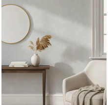 Lichtgrijze wand in een woonkamer met houten sidetable, ronde spiegel en beige fauteuil.