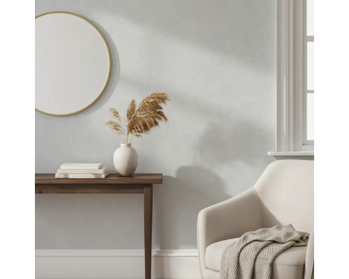 Lichtgrijze wand in een woonkamer met houten sidetable, ronde spiegel en beige fauteuil.