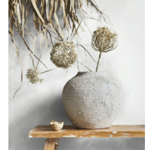 Ronde keramieken vaas met ruwe textuur en droogbloemen op een houten bankje voor een lichte wand.