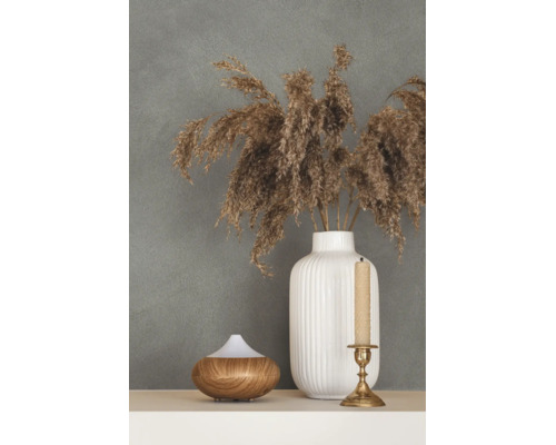 Decoratieve opstelling met een witte geribbelde keramische vaas, gedroogd pampasgras, een diffuser in houtoptiek en een kandelaar voor een wand met textuur.