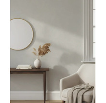 Licht ingerichte woonkamer met beige muur, ronde spiegel, donkere consoletafel, witte vaas en een comfortabele fauteuil.