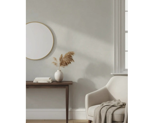 Licht ingerichte woonkamer met beige muur, ronde spiegel, donkere consoletafel, witte vaas en een comfortabele fauteuil.
