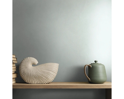Moderne kamer met matgroen geschilderde muur, houten wandplank, decoratieve schelpvormige sculptuur en een groene keramische theepot.