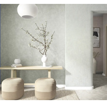 Lichte kamer met structuurwand, houten console, twee gevlochten poefs, vloerkleed en vaas met bloesemtakken.