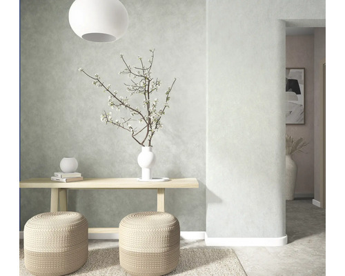 Lichte kamer met structuurwand, houten console, twee gevlochten poefs, vloerkleed en vaas met bloesemtakken.