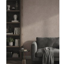 Moderne woonkamer met een roze muur met structuur, een donkergroene fluwelen bank en een donkere houten boekenkast met boeken en decoratie.