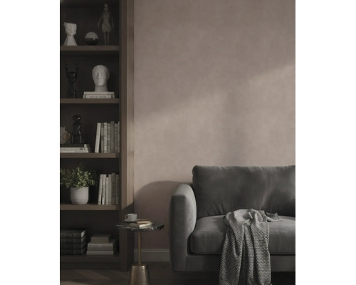 Moderne woonkamer met een roze muur met structuur, een donkergroene fluwelen bank en een donkere houten boekenkast met boeken en decoratie.