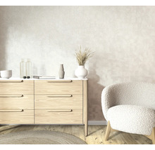 Lichte woonruimte met behang met structuur, een moderne houten ladekast en een zachte fauteuil op een lichte parketvloer.