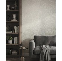 Gestructureerd vliesbehang in een moderne woonkamer achter een grijze bank en naast een donkere houten boekenkast.