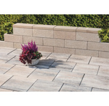Licht terras met gestructureerde, rechthoekige vloertegels en een lage tuinmuur van betonblokken.