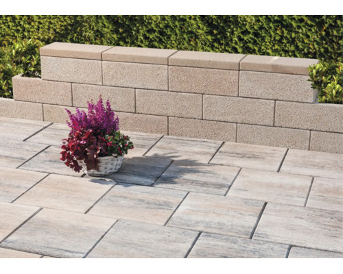 Licht terras met gestructureerde, rechthoekige vloertegels en een lage tuinmuur van betonblokken.